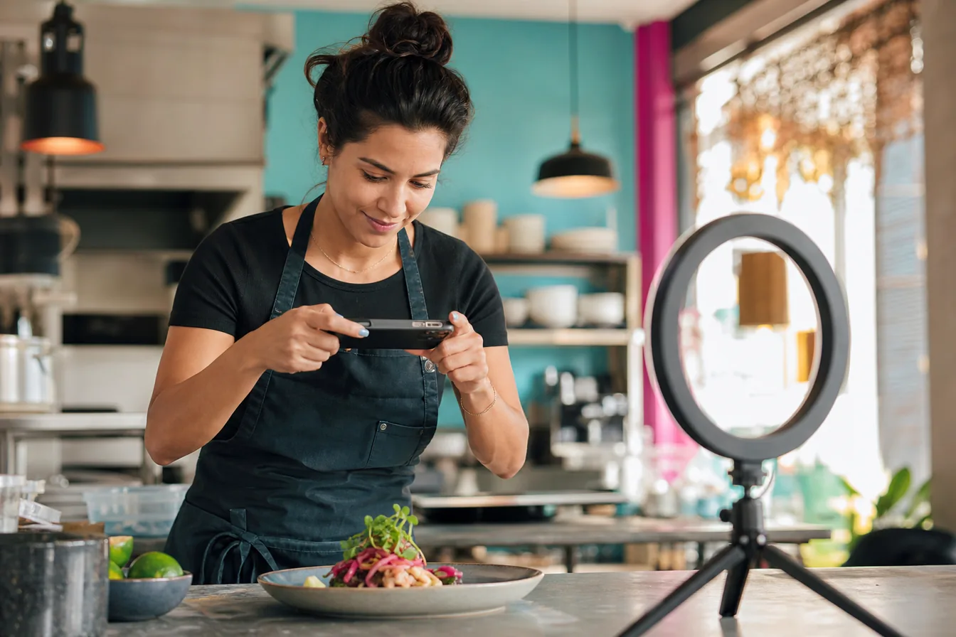 Restaurant owner photographing a plated dish with her phone using a ring light — illustrative photo