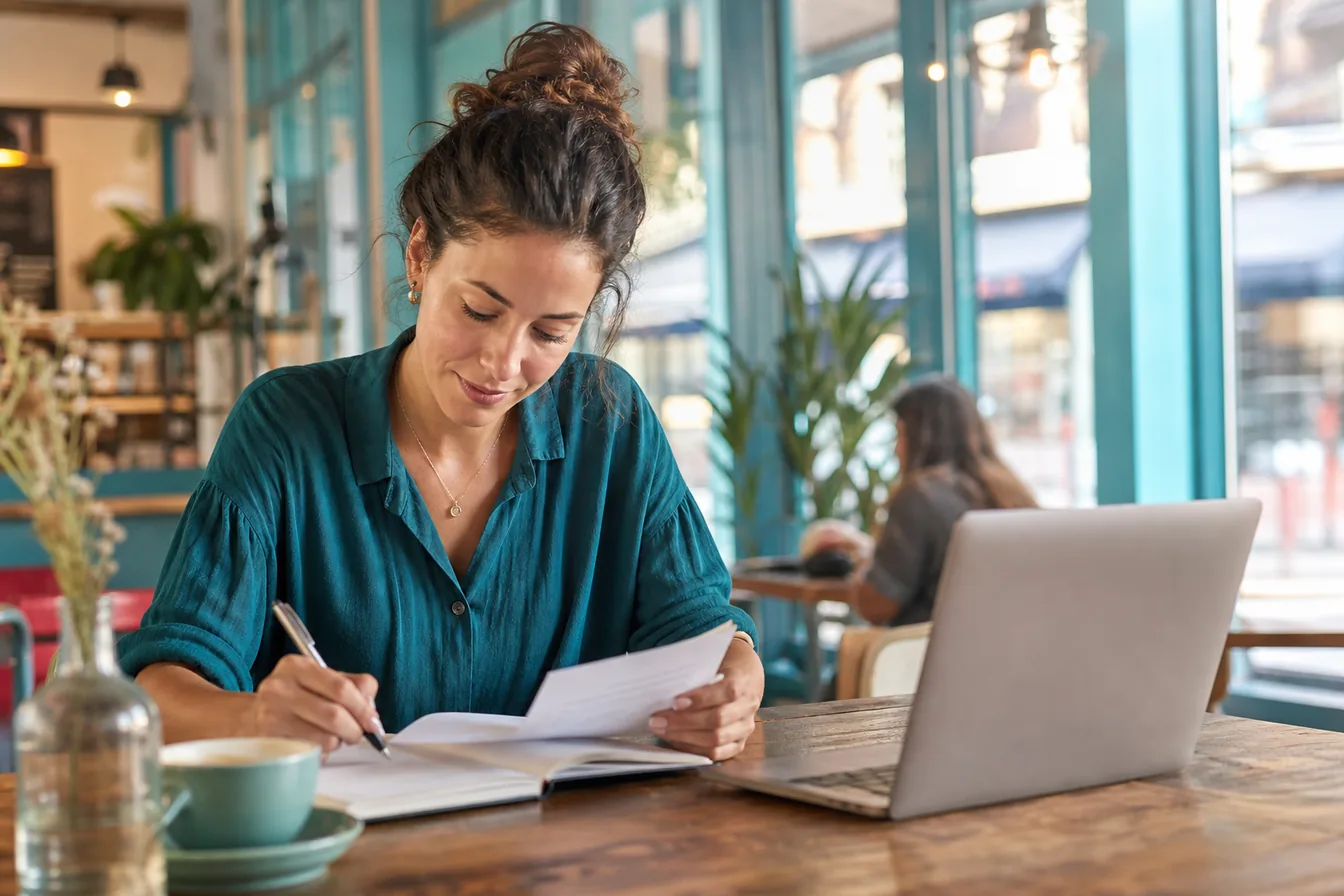 Business owner taking notes at a sunlit table while researching her website — illustrative photo