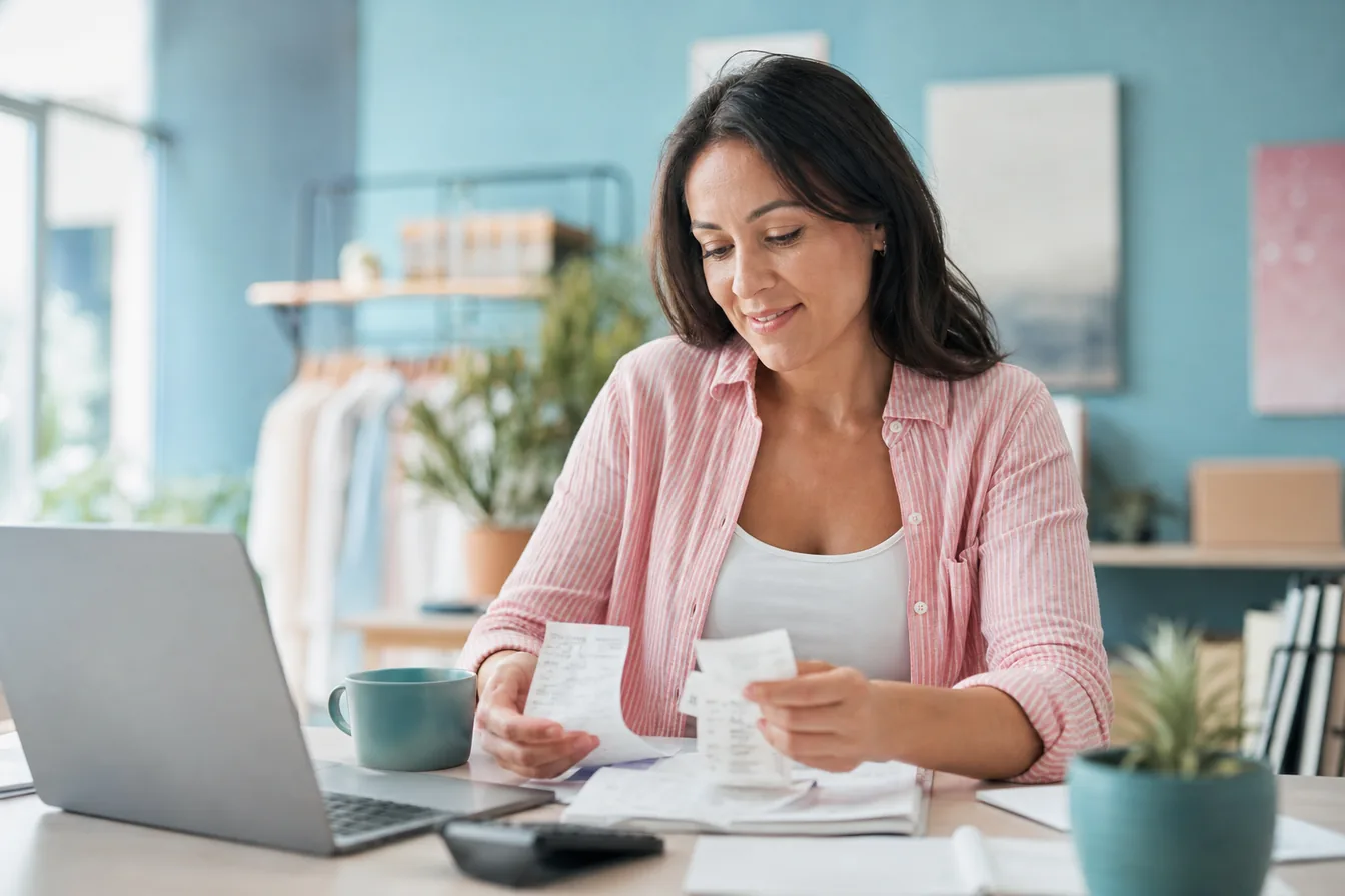 Business owner sorting receipts beside a laptop while reviewing her monthly budget — illustrative photo for monthly website costs