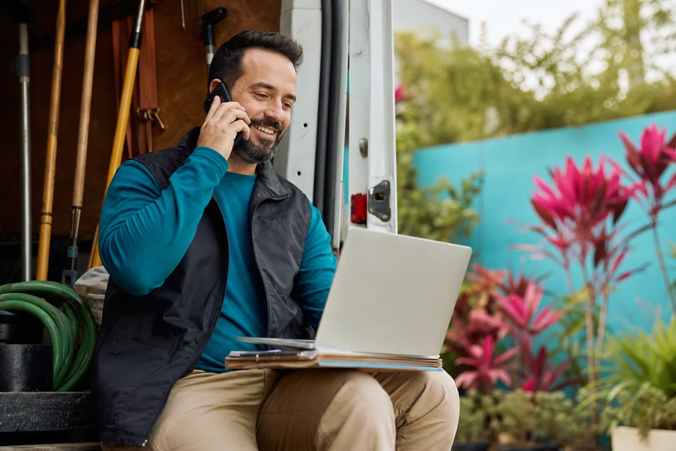 Landscaping business owner on a phone call with a laptop open — illustrative photo