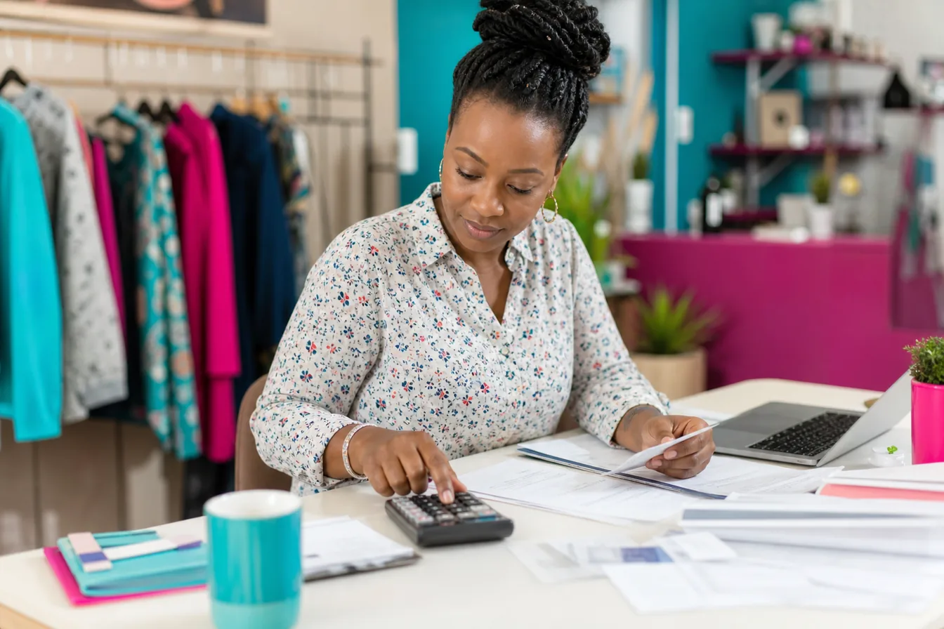 Business owner reviewing monthly expenses with a calculator and laptop — illustrative photo