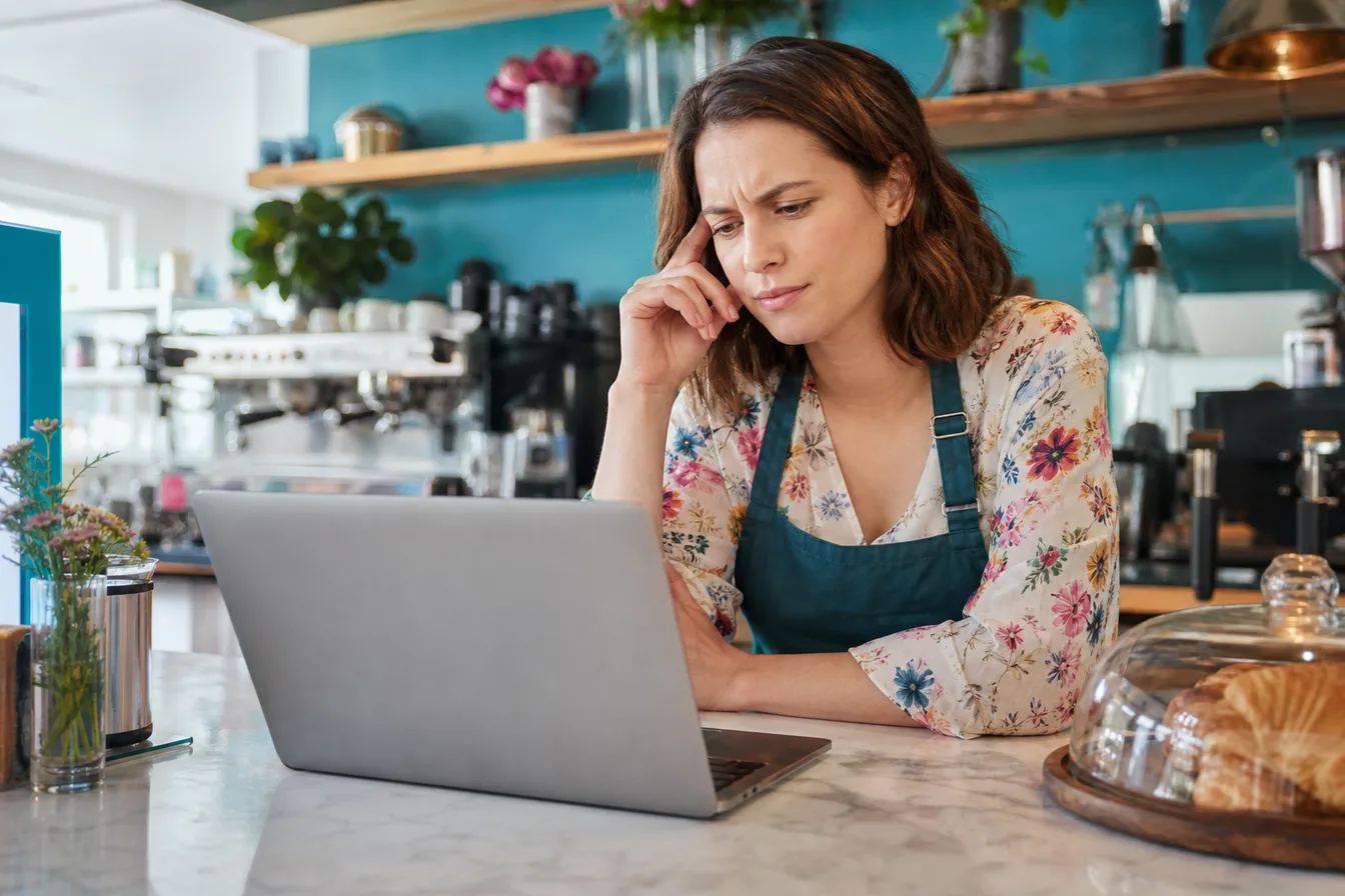 Cafe owner looking puzzled at her laptop at the counter — illustrative photo
