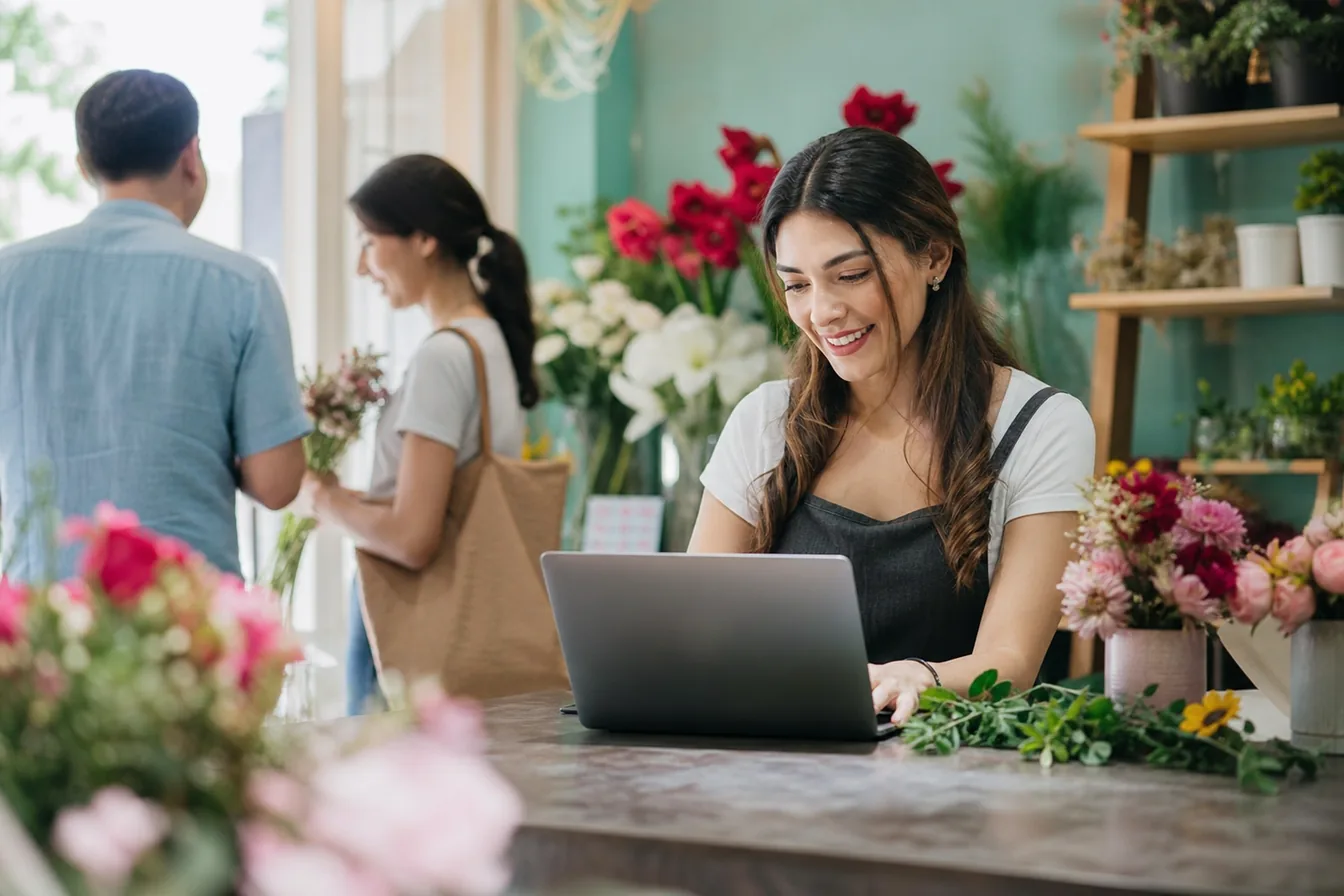Florist updating her website on a laptop at the flower shop counter — illustrative photo