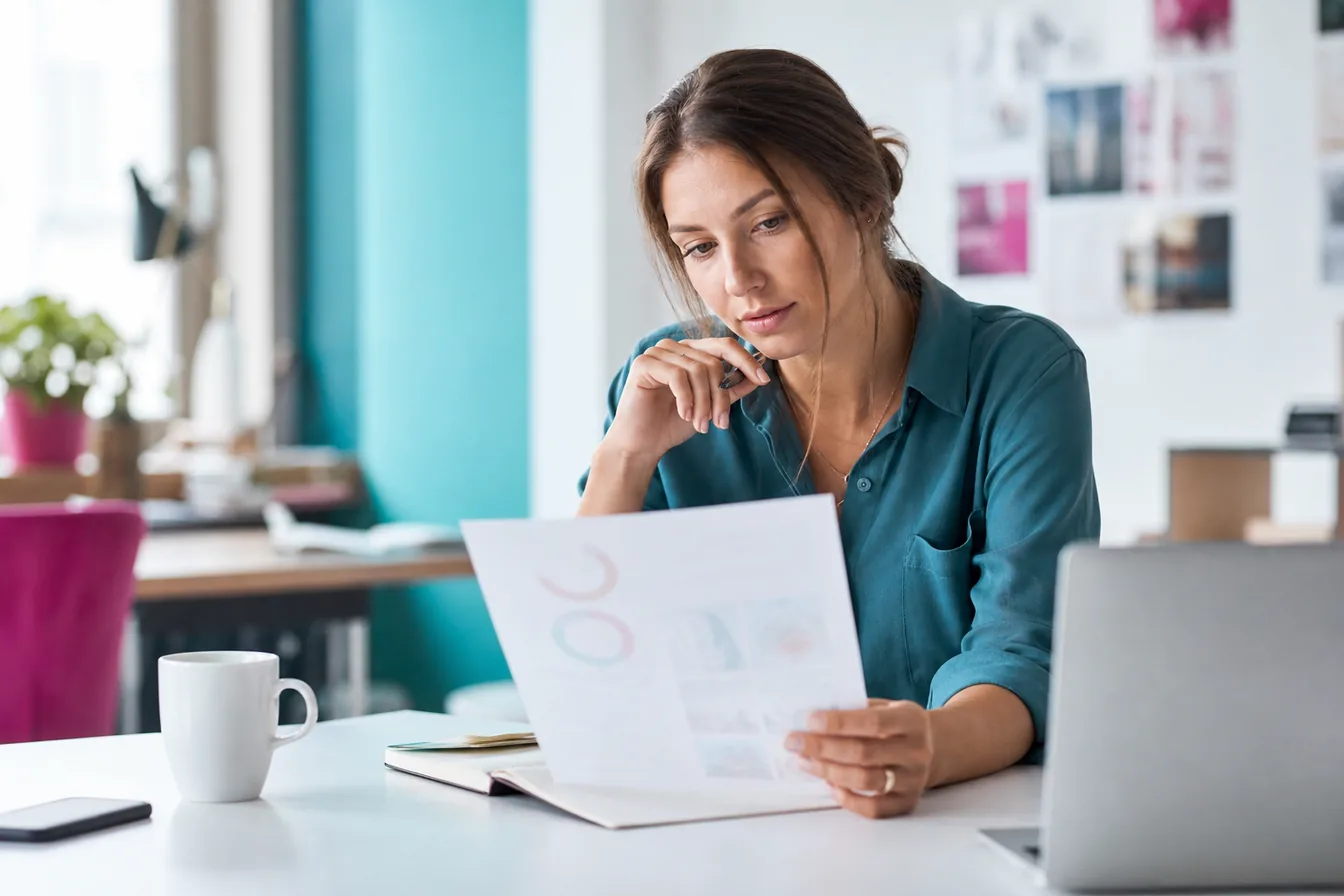 Marketer reviewing a single printed page layout at a desk, pen in hand — illustrative photo