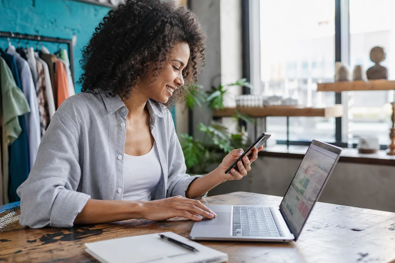 Person comparing a website on a phone and a laptop side by side — illustrative photo