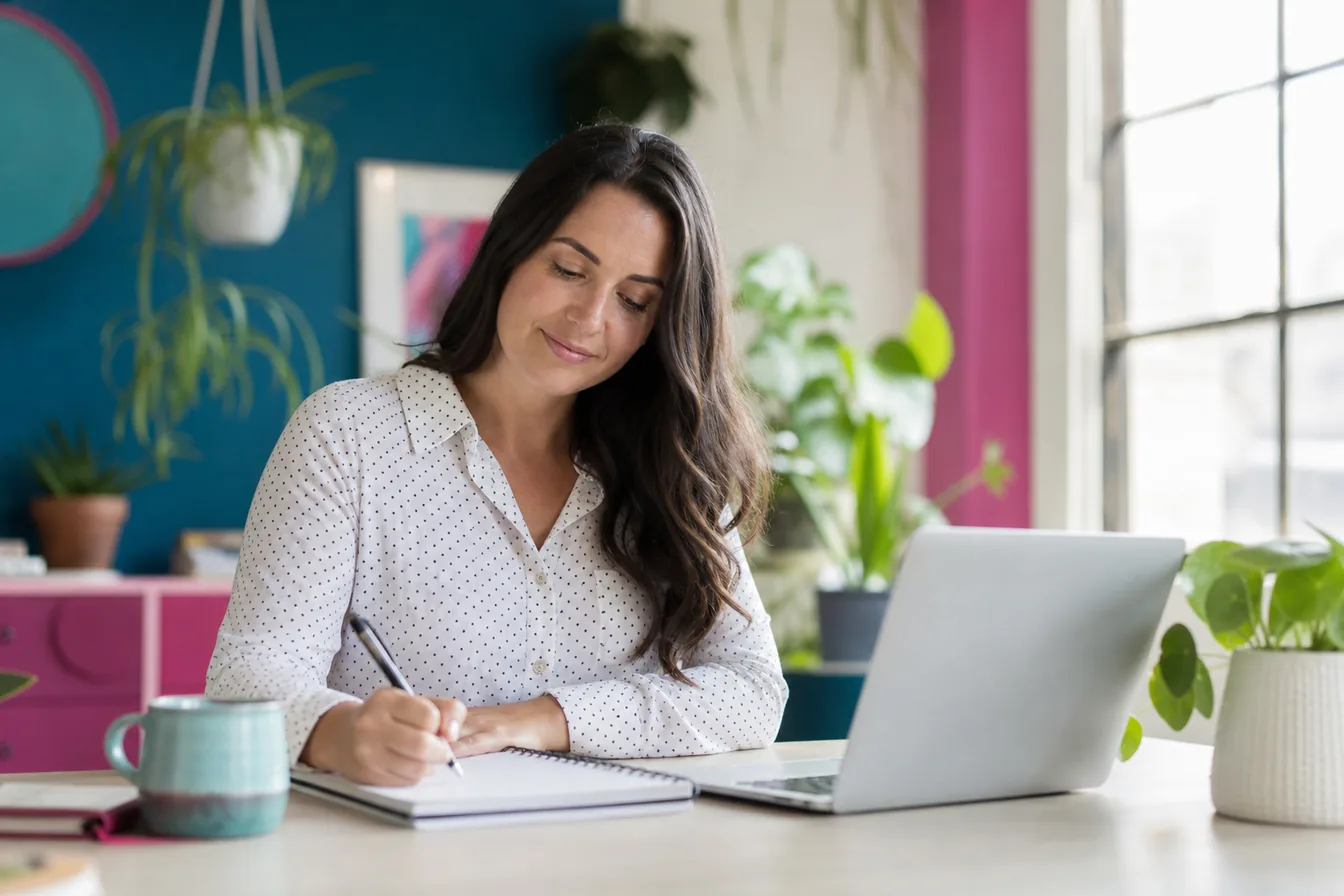 Business owner drafting website content in a notebook beside a laptop — illustrative photo